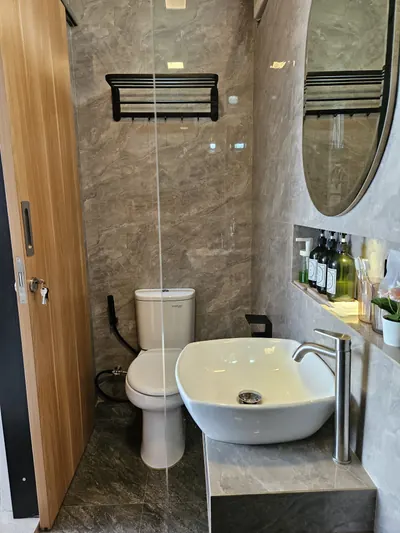 Kamar mandi dengan wastafel bulat, cermin oval, dan dinding bermotif marmer