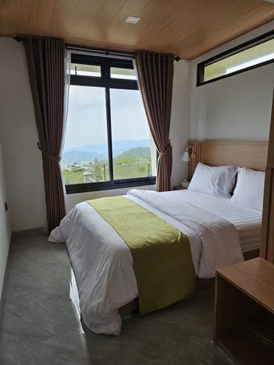 Kamar tidur dengan king bed, langit-langit kayu, dan jendela lebar menghadap perbukitan