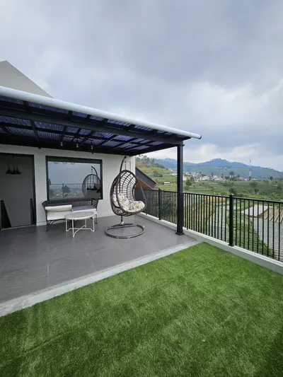 Rooftop berumput dengan kursi ayun rotan dan pagar, menghadap perbukitan kaki Gunung Slamet
