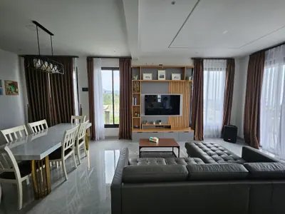 Ruang keluarga villa dengan sofa L, Smart TV, dan meja makan di belakangnya
