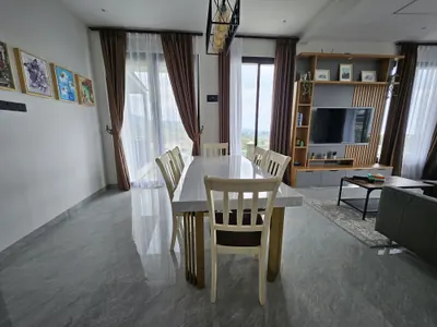 Meja makan kayu untuk enam orang di ruang terbuka villa, bersambung ke ruang keluarga
